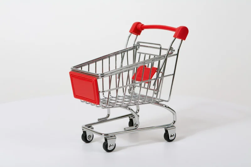 Miniature empty shopping cart with red plastic handle on white surface