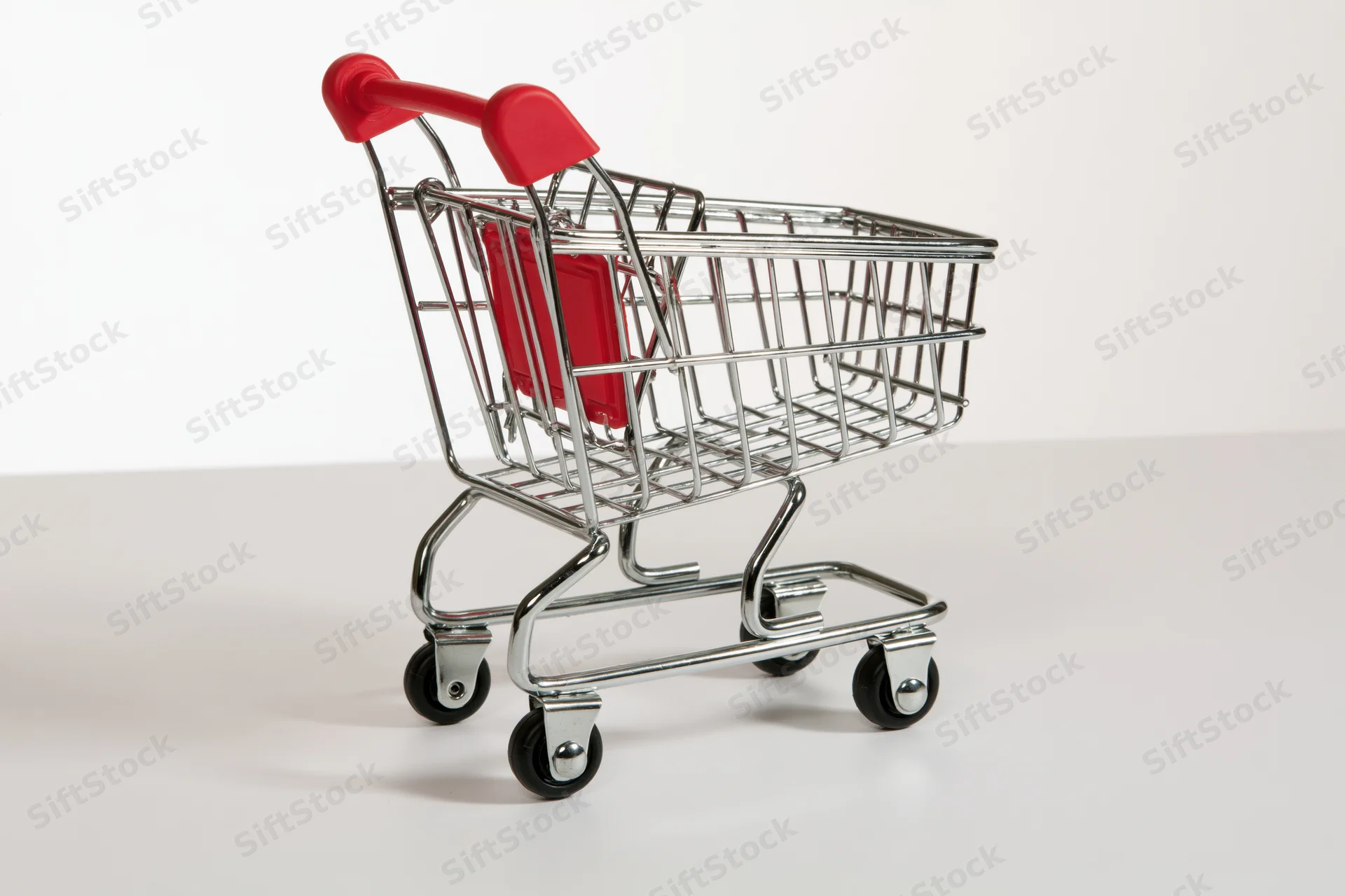 Miniature empty shopping cart with red plastic handle on white surface