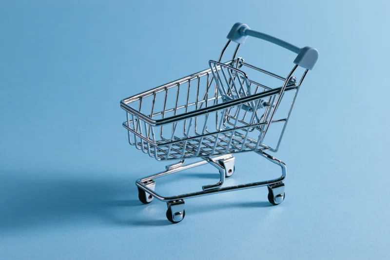 Miniature metal shopping cart empty on blue background with copyspace