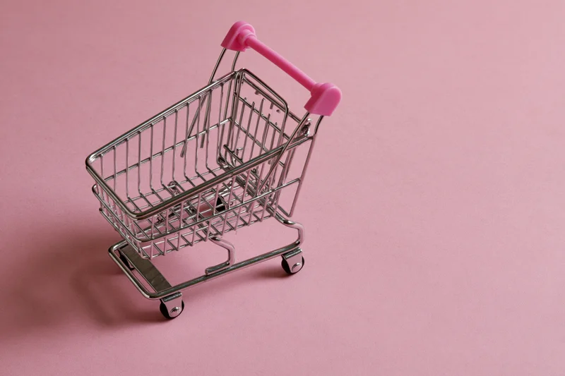 Miniature metal shopping cart with pink plastic handle on pink surface