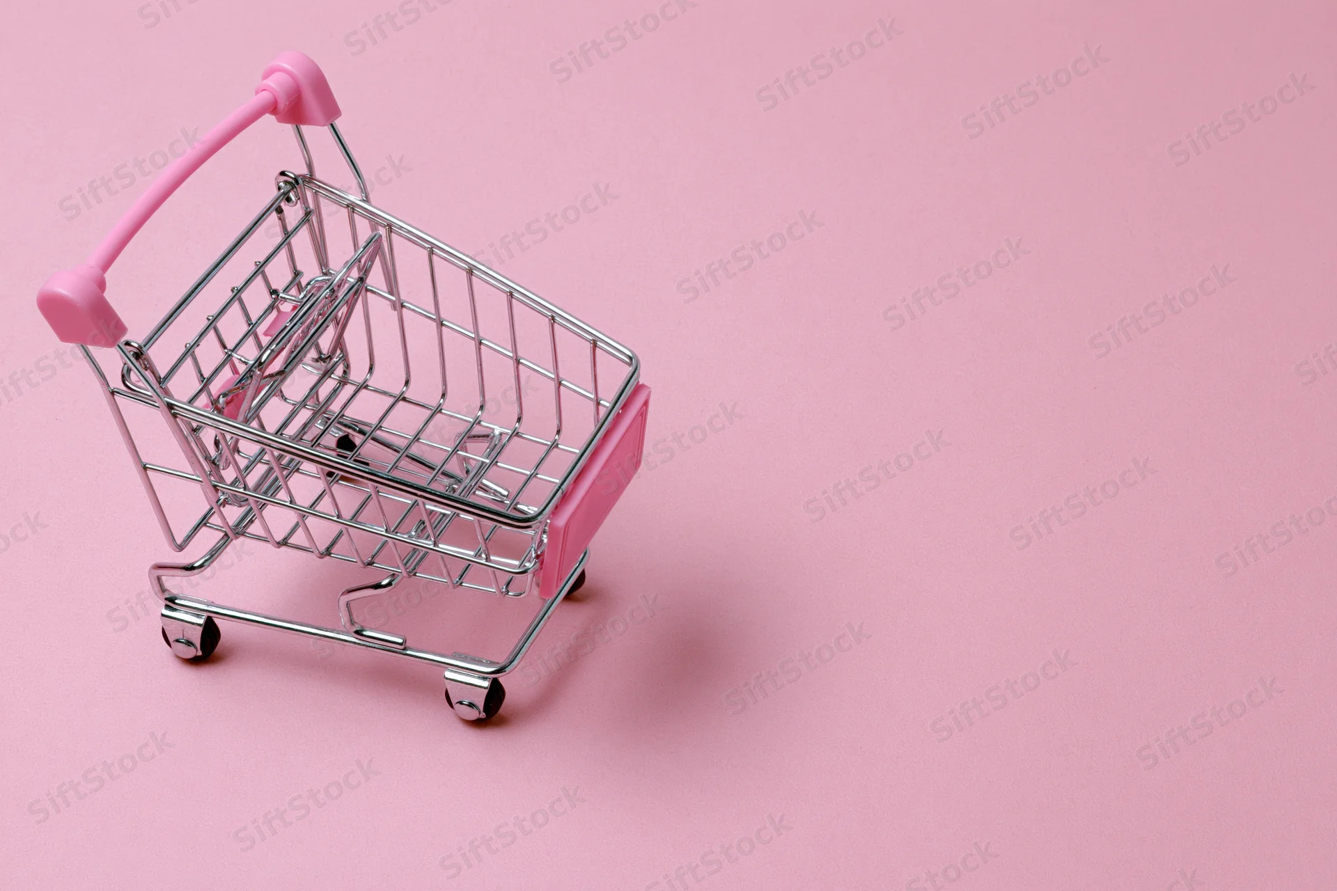 Miniature metal shopping cart with pink plastic handle on pink surface