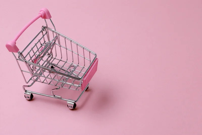 Miniature metal shopping cart with pink plastic handle on pink surface