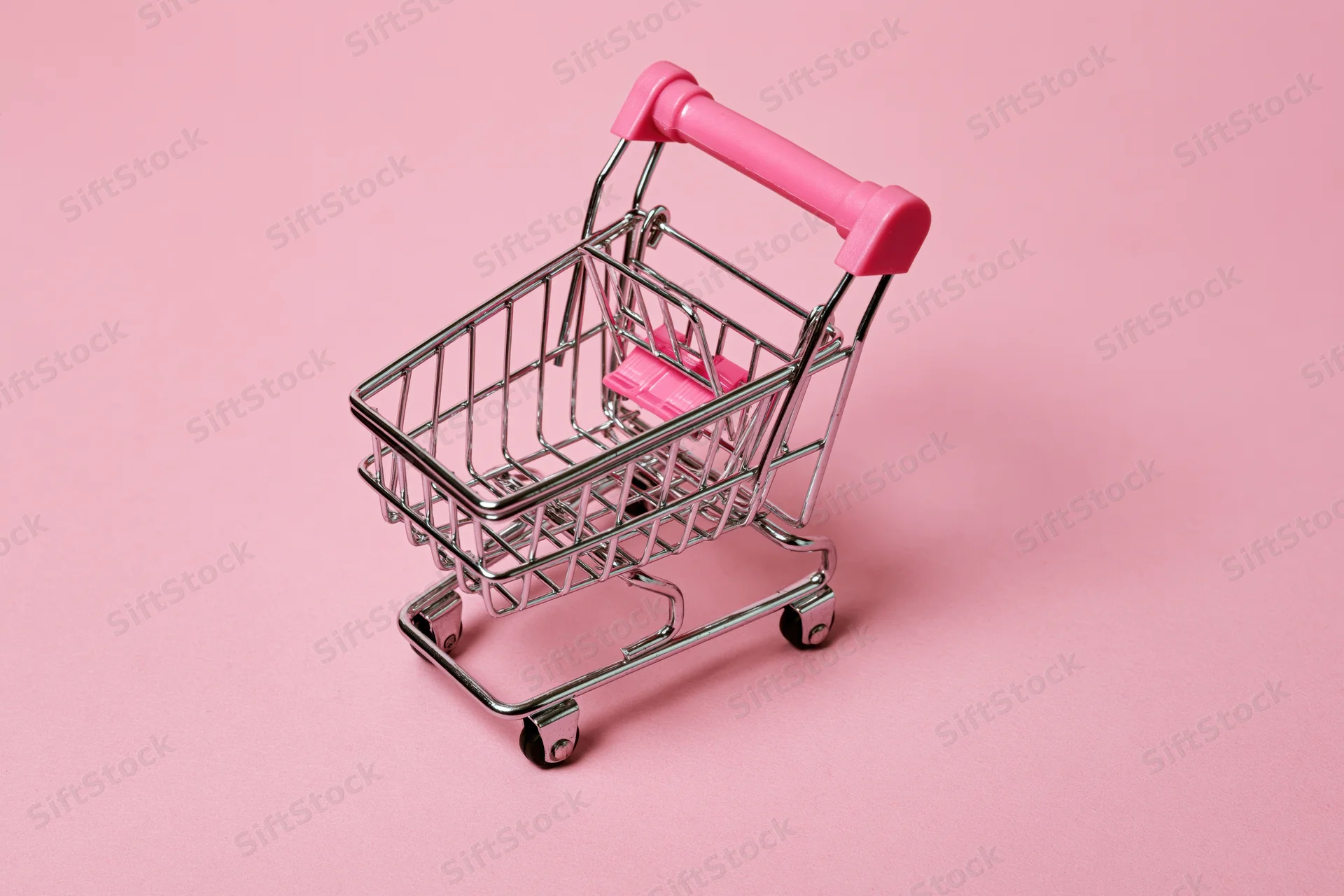 Miniature metal shopping cart with pink plastic handle on pink background