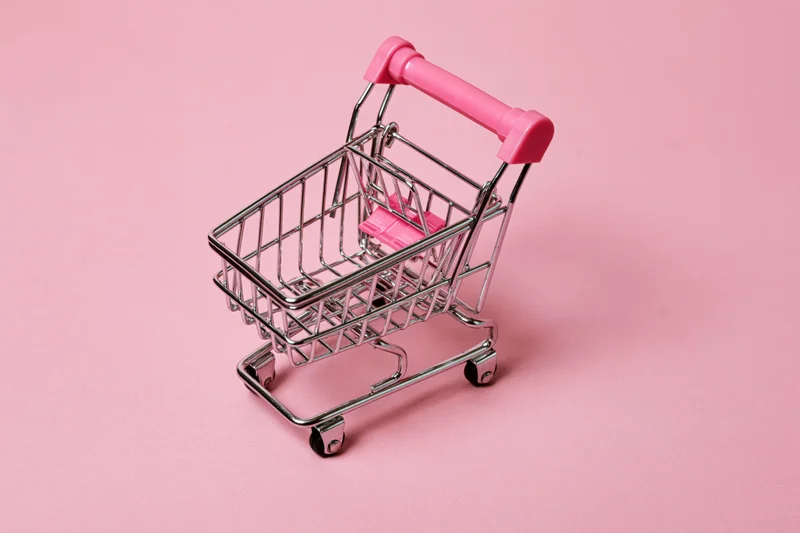 Miniature metal shopping cart with pink plastic handle on pink background