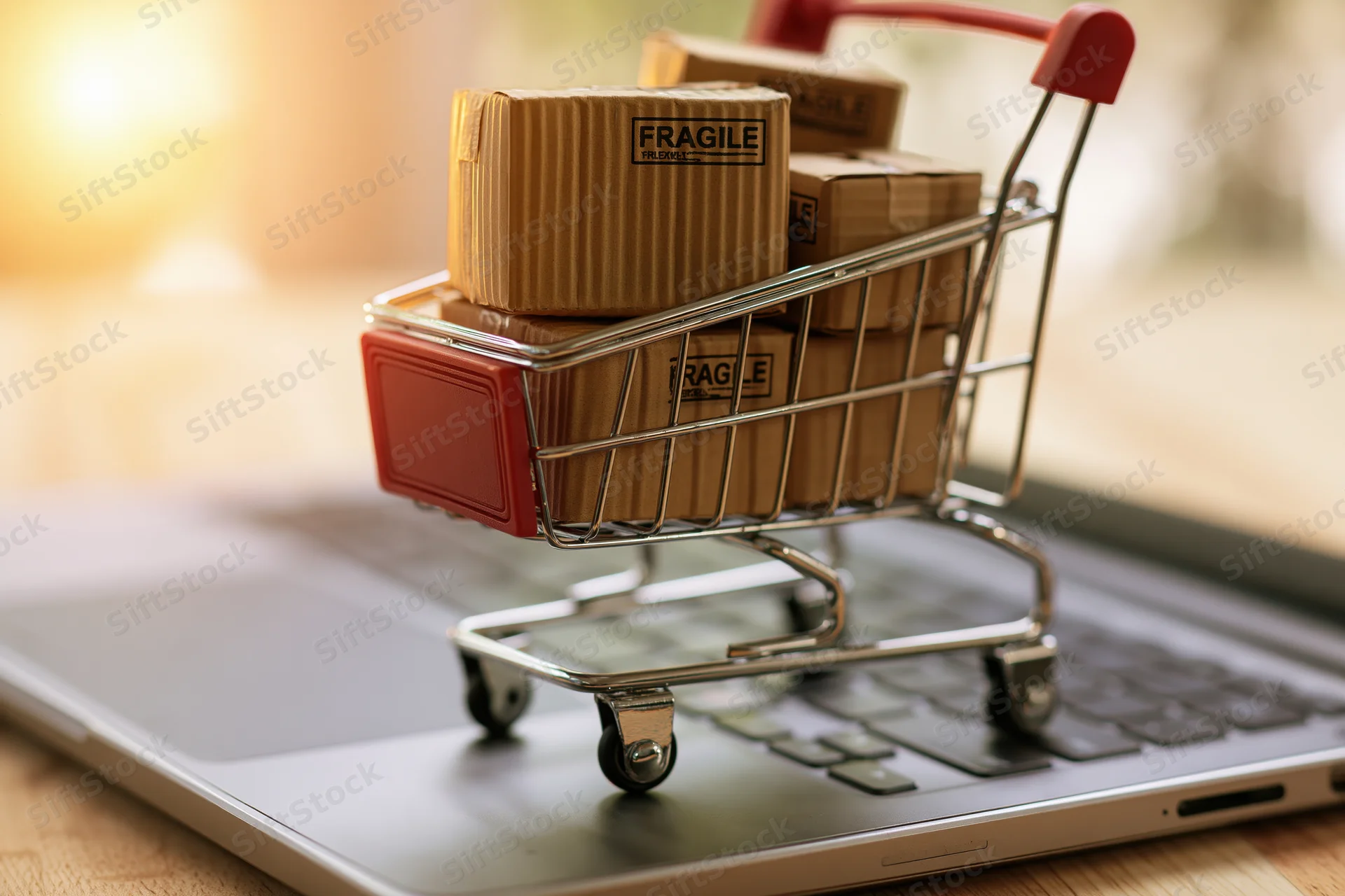 Miniature shopping cart filled with fragile cardboard boxes resting on a laptop keyboard