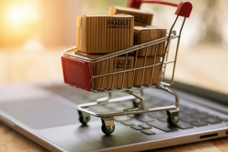 Miniature shopping cart filled with fragile cardboard boxes resting on a laptop keyboard