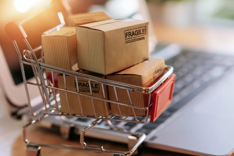 Small metal shopping cart filled with cardboard boxes labeled fragile resting on a laptop keyboard