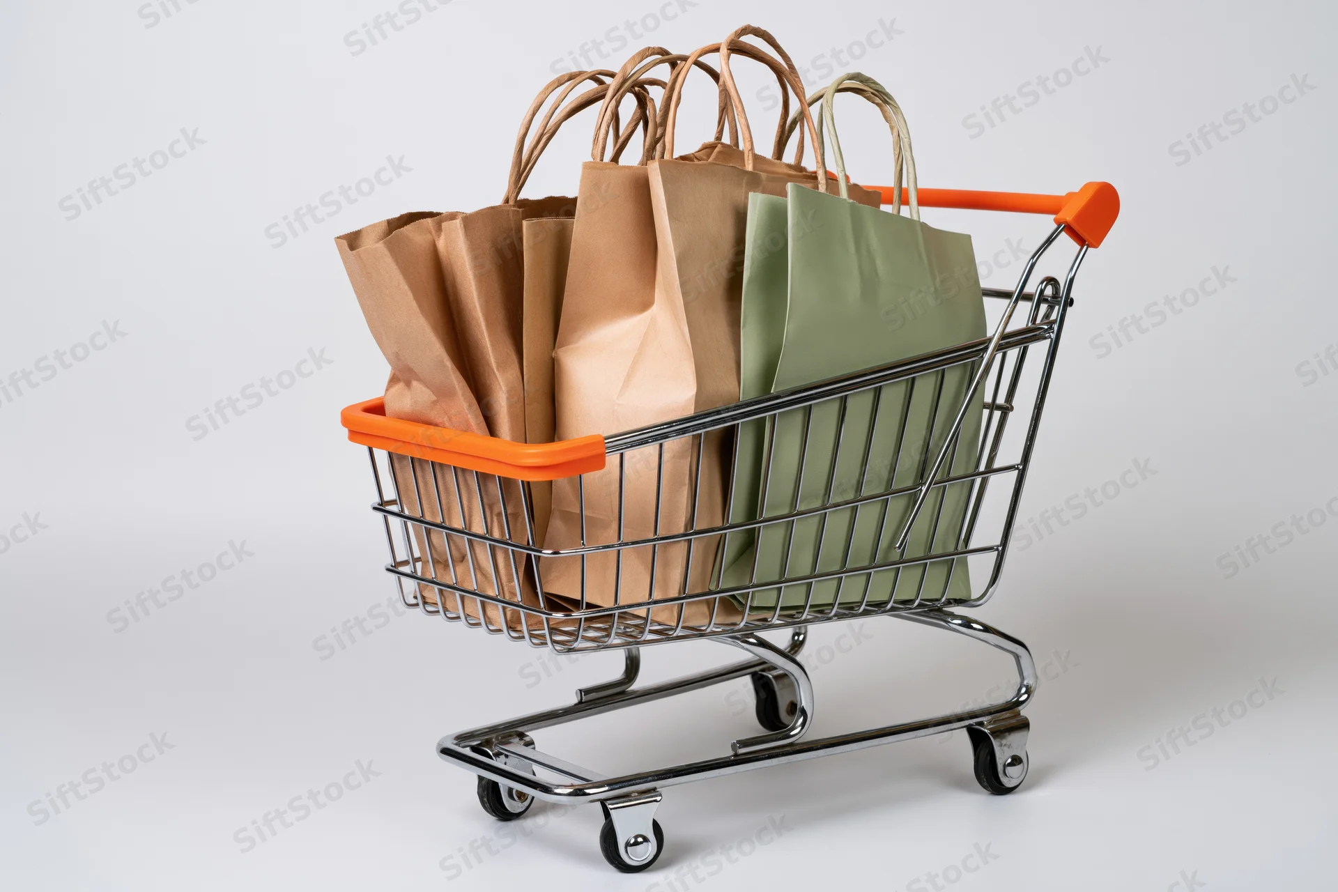Small metal shopping cart with orange trim filled with brown and green paper bags on white background