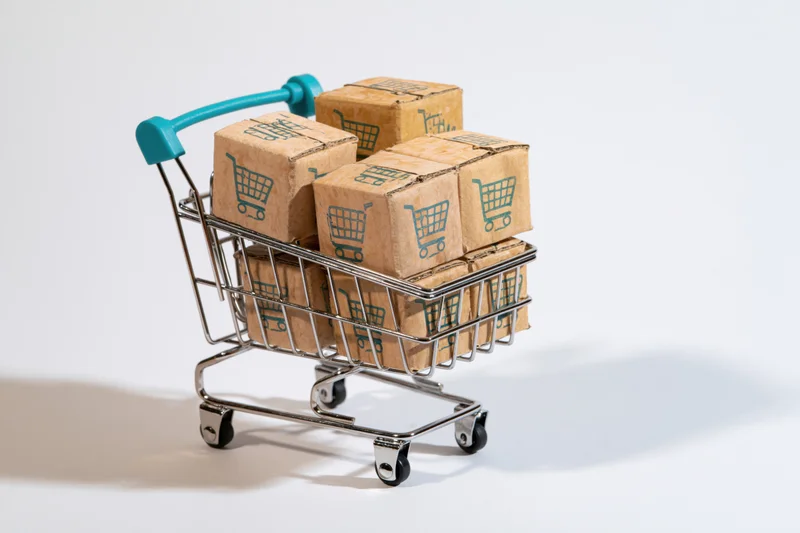 Miniature shopping cart filled with cardboard boxes printed with shopping cart symbols on white background