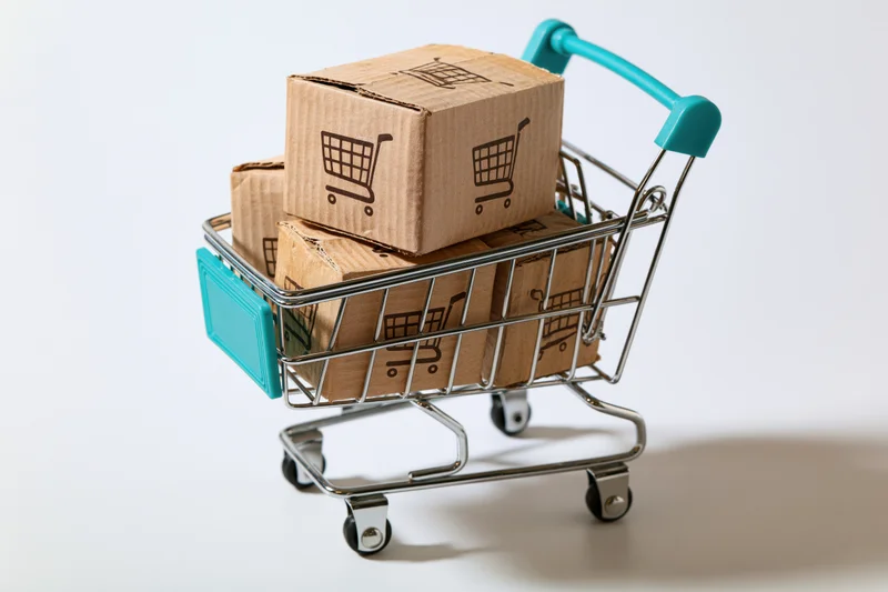 Small metal shopping cart filled with cardboard boxes printed with shopping cart symbols on white background