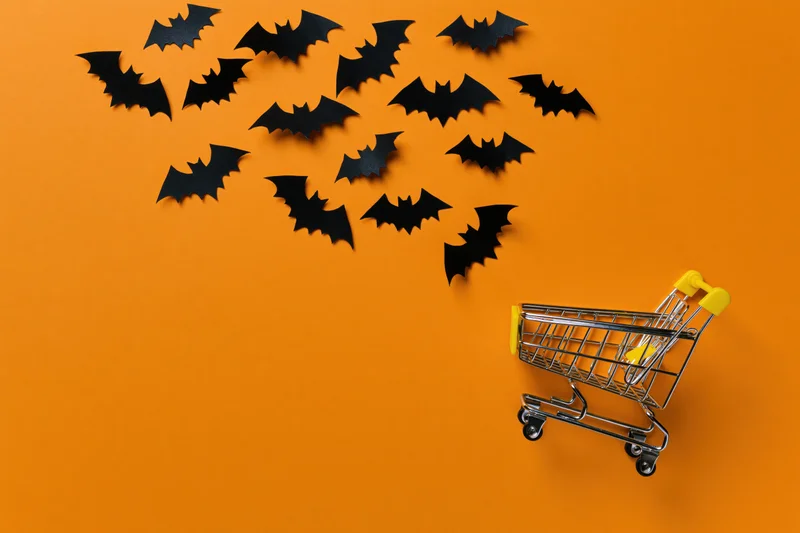 Miniature shopping cart with paper bats on orange background