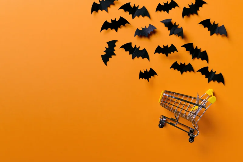 Miniature shopping cart with paper bats flying above on orange background