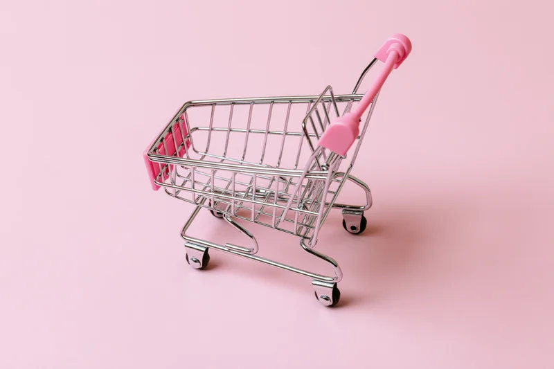 Miniature silver shopping cart with pink plastic handle on a pink background