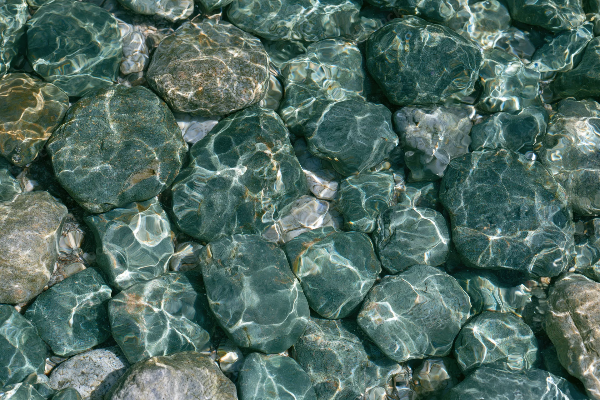 Smooth river stones submerged under clear shallow water with light ripples and reflections