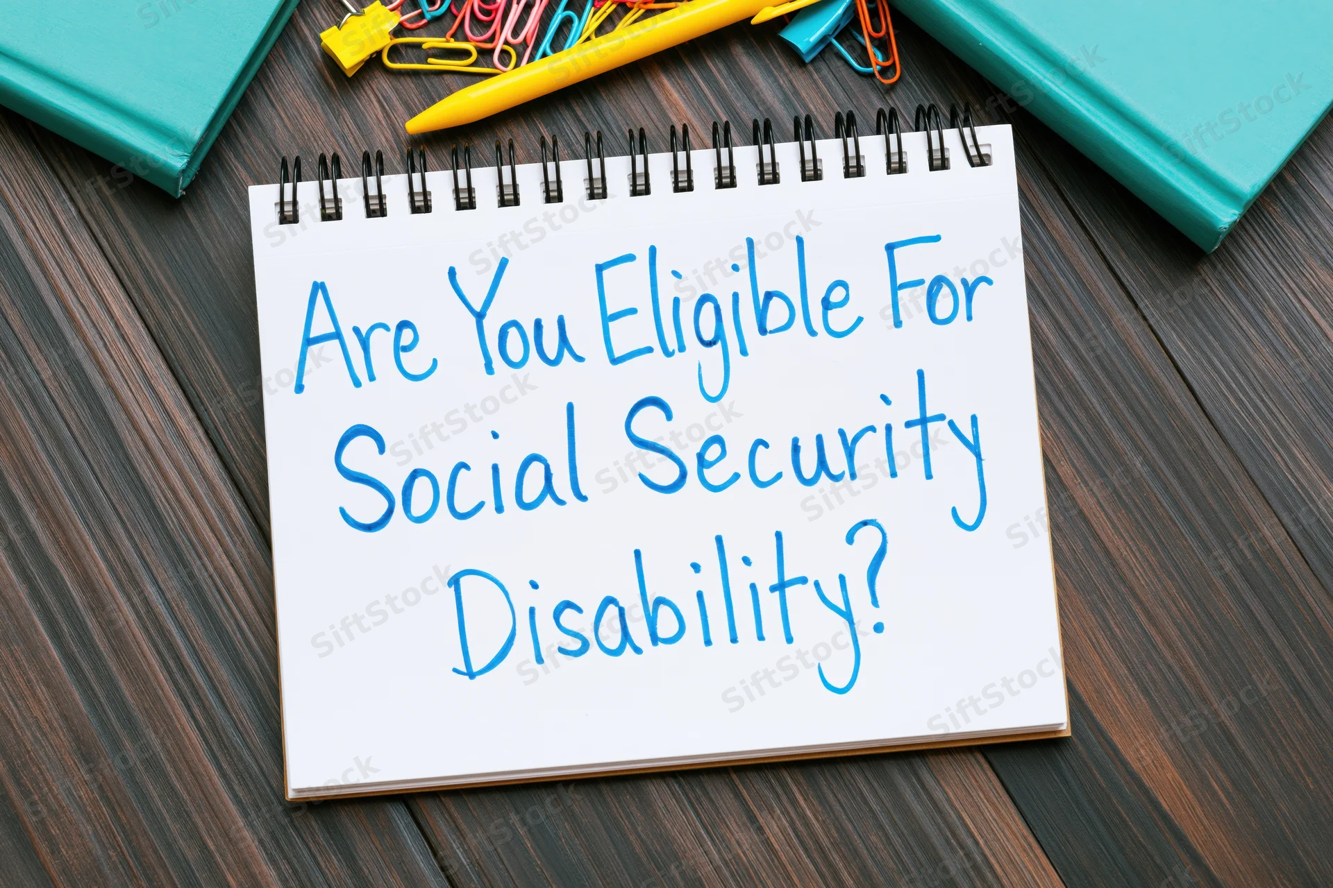 Spiral-bound notepad with handwritten question about social security disability eligibility on dark wood desk