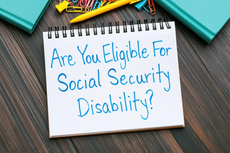 Spiral-bound notepad with handwritten question about social security disability eligibility on dark wood desk