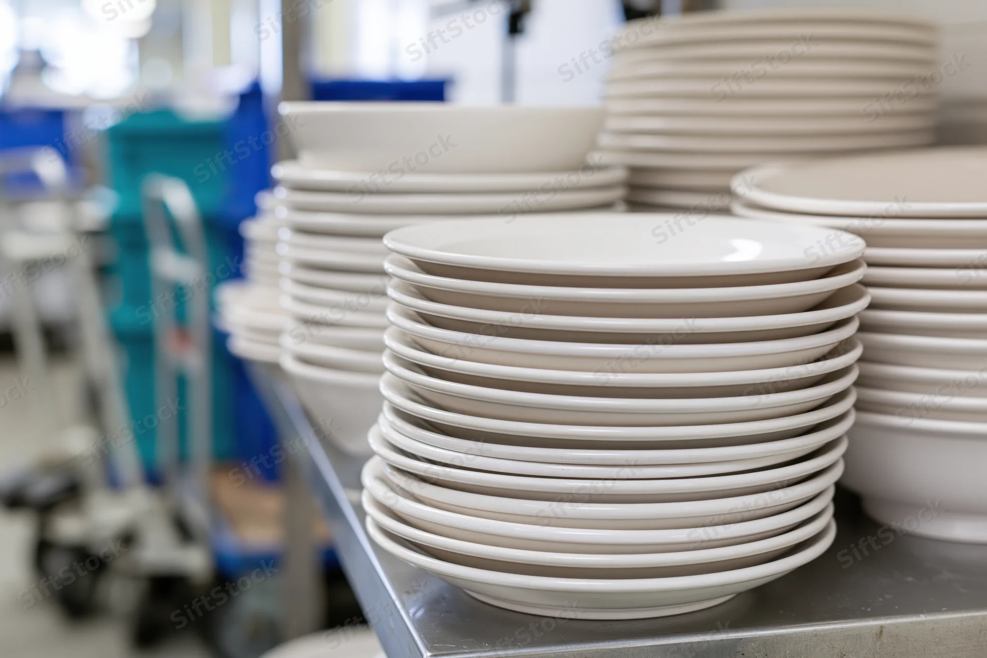 Stacks of clean white ceramic plates and bowls piled on a metal shelf in a commercial kitchen