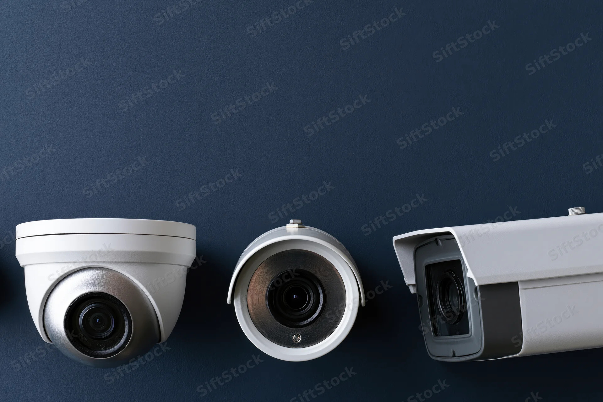 Three cctv security cameras mounted on a dark blue wall in a row