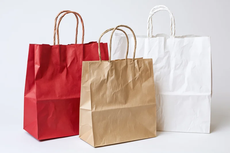 Three paper shopping bags in red, brown and white arranged together on a white background