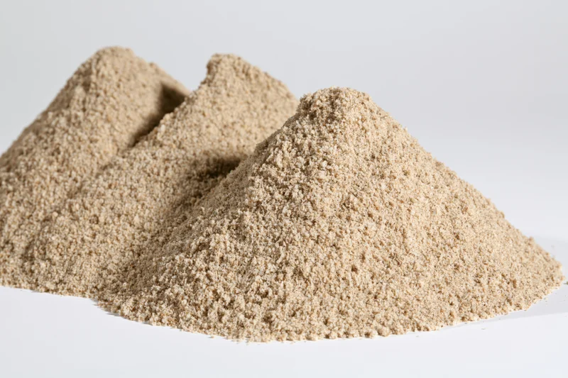 Three small mounds of dry construction sand piled together on a white surface