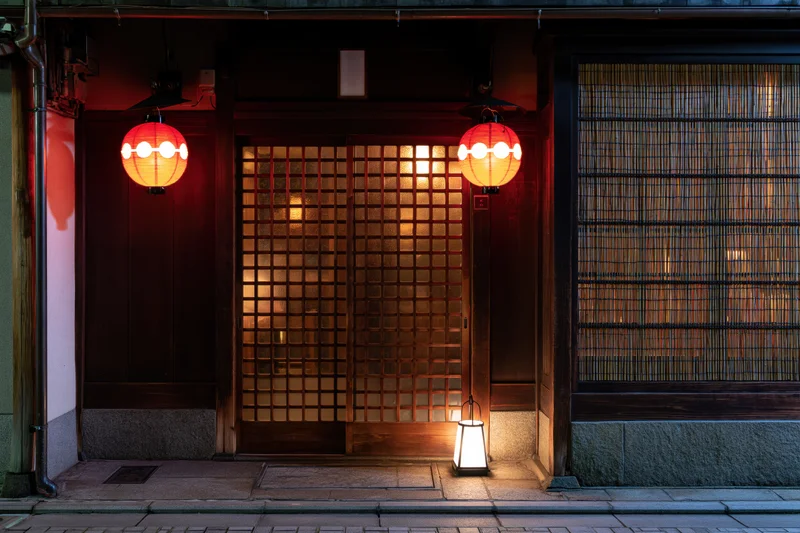 Traditional japanese restaurant entrance at night with glowing red lanterns and wooden grid door