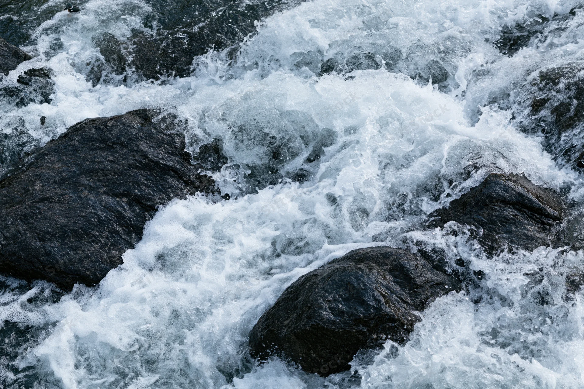 Turbulent river rapids crashing over dark wet rocks in a mountain stream