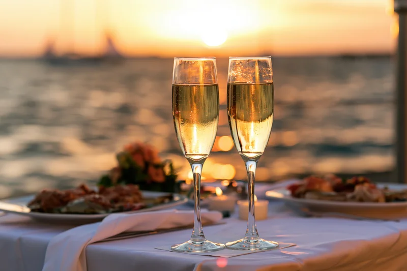 Two champagne flutes on a table set for dinner by the ocean at sunset