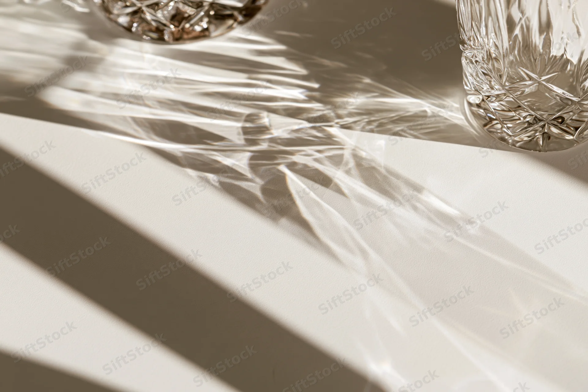 Cut crystal glasses casting intricate light patterns and shadows on a white surface
