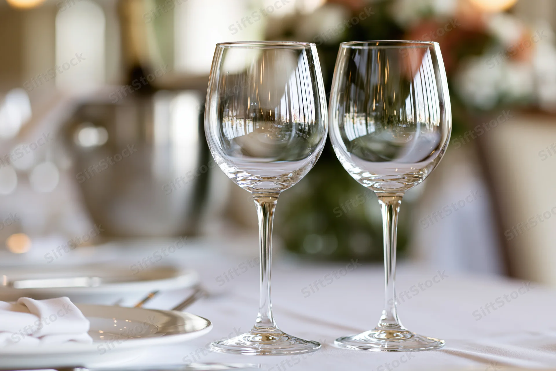 Two empty crystal wine glasses on a formally set dining table with floral centerpiece and white linens