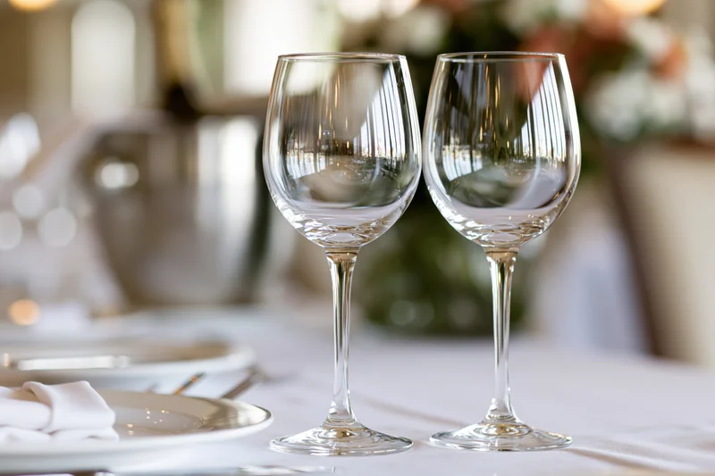 Two empty crystal wine glasses on a formally set dining table with floral centerpiece and white linens