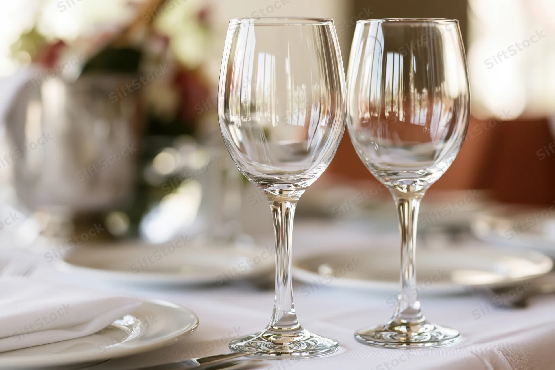 Two empty crystal wine glasses on a formally set dining table with plates, napkins and floral centerpiece