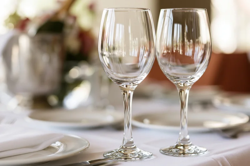 Two empty crystal wine glasses on a formally set dining table with plates, napkins and floral centerpiece