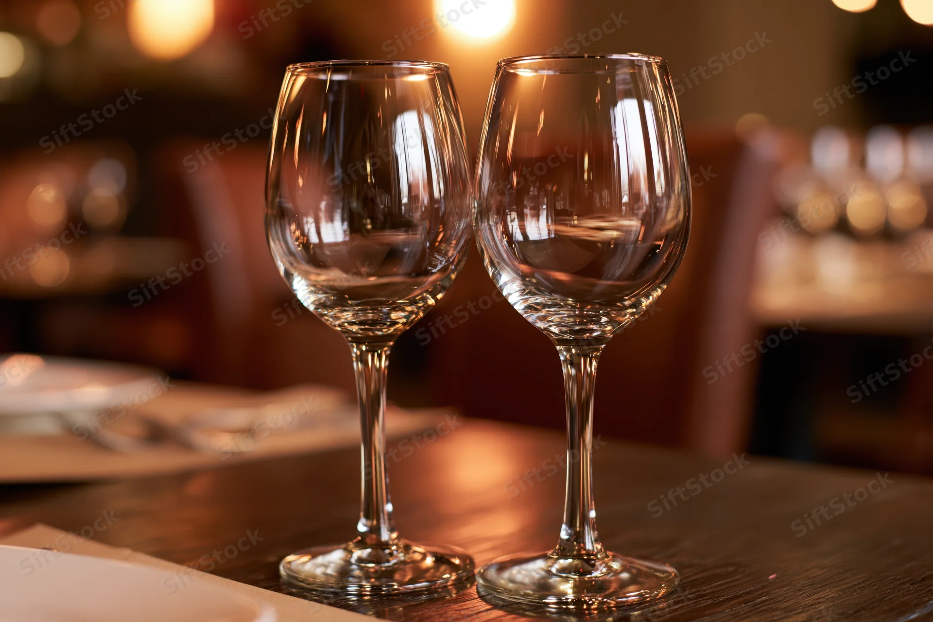 Two empty wine glasses on a dark wooden restaurant table