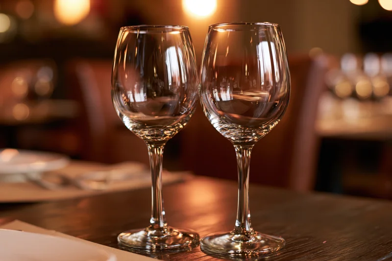 Two empty wine glasses on a dark wooden restaurant table