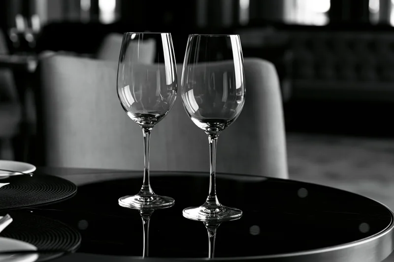 Two empty wine glasses on a glossy black table in a formal restaurant setting