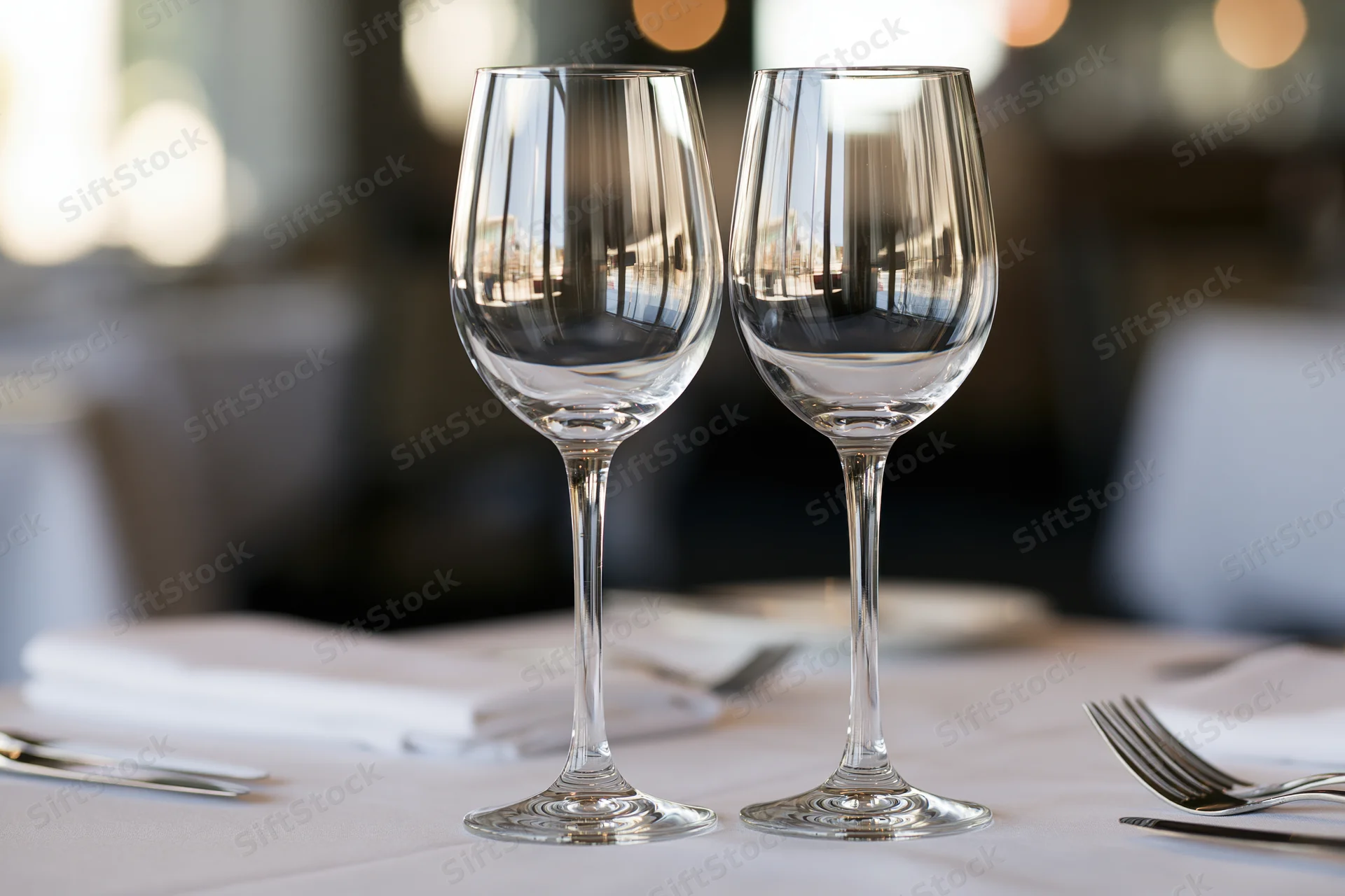 Two empty wine glasses on a white-linen restaurant table with silverware and napkins arranged for dining