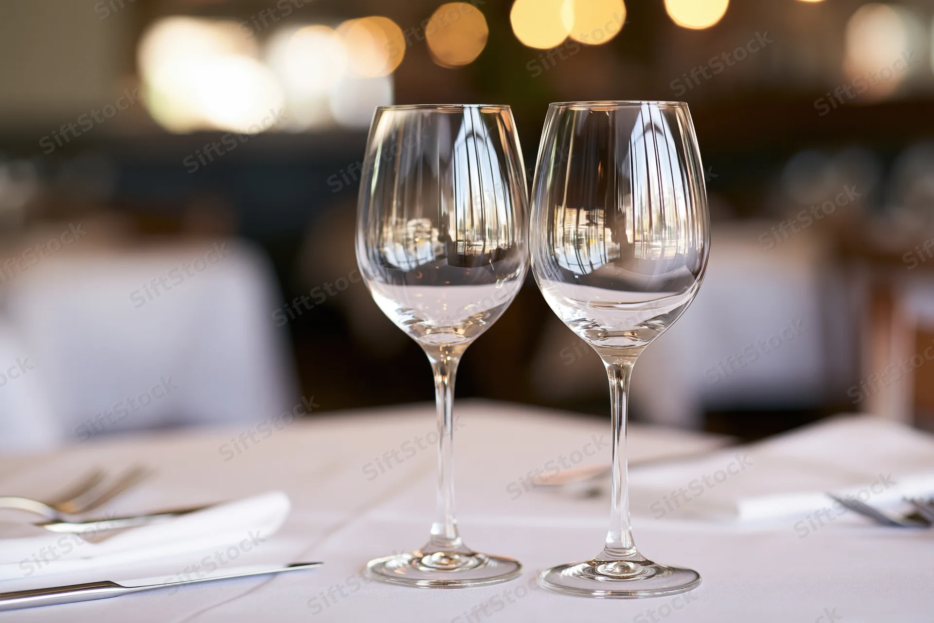 Two empty wine glasses on a white-linen table in a restaurant dining room