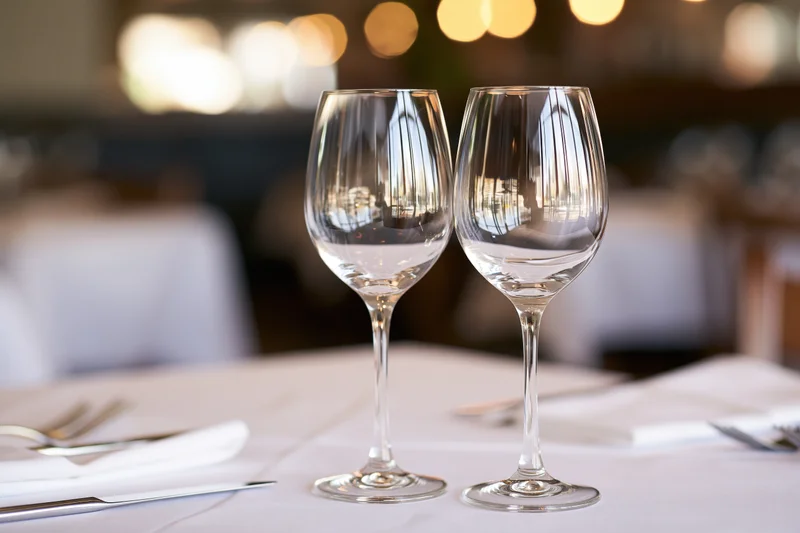 Two empty wine glasses on a white-linen table in a restaurant dining room
