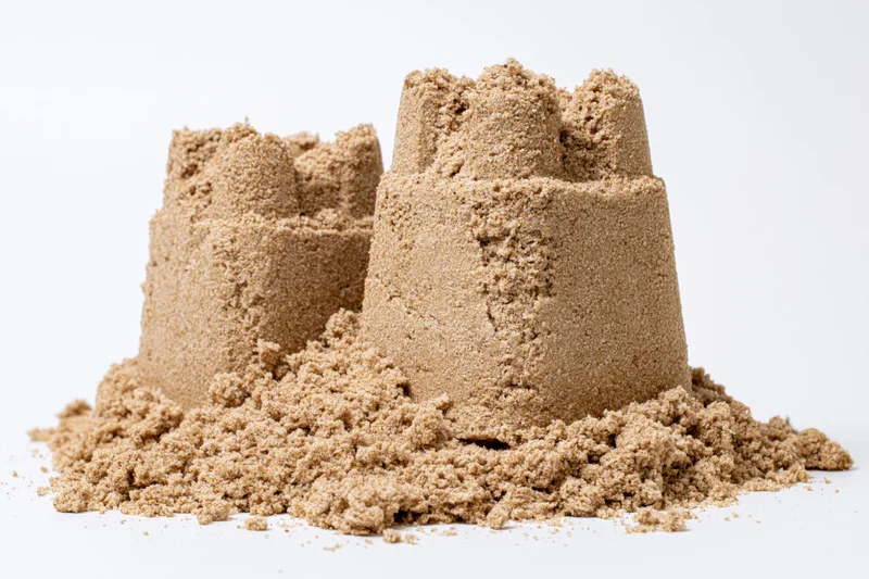 Two handmade sand castles of different heights on a white surface