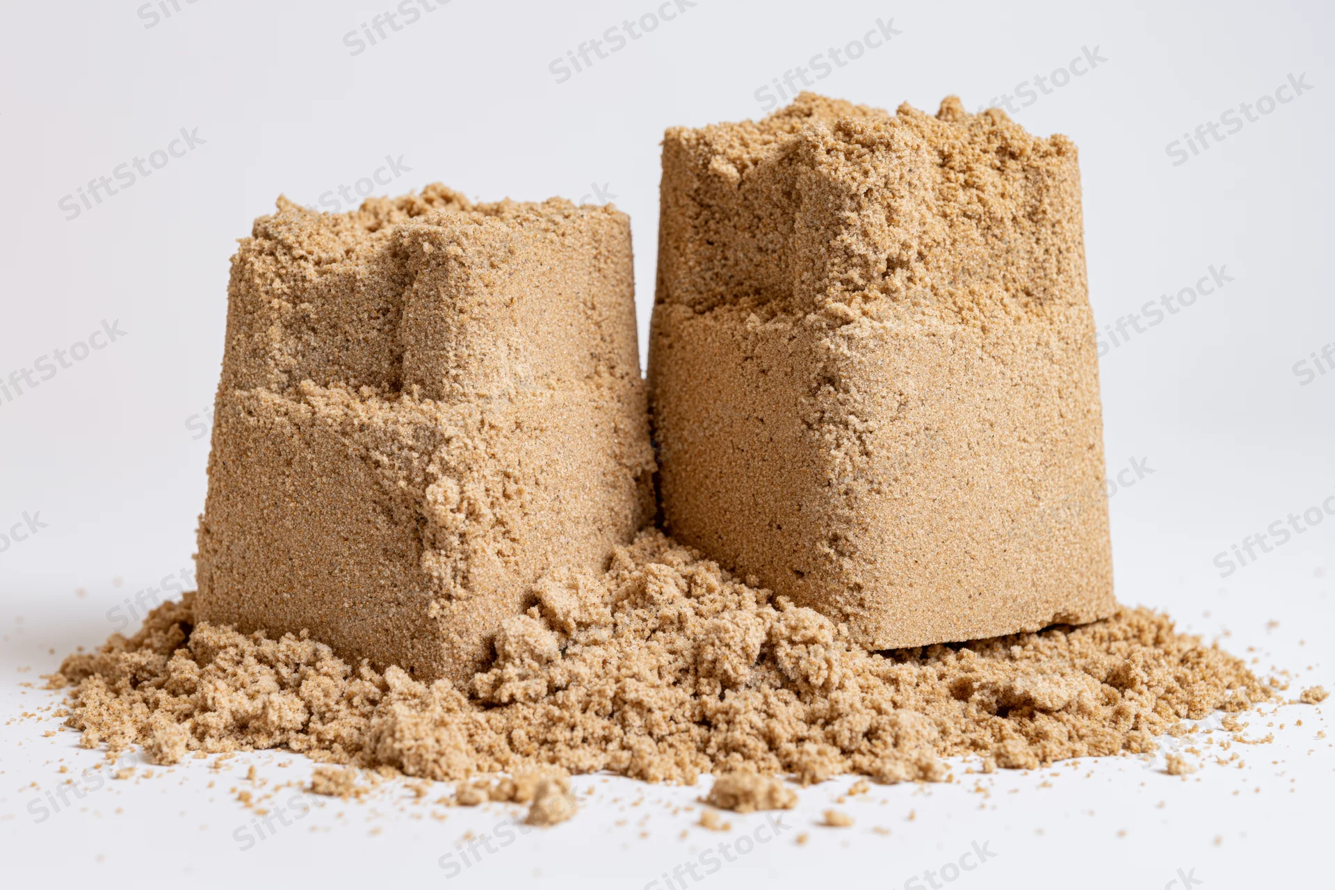Two handmade sand castles of different heights sitting on a white surface with scattered sand around them