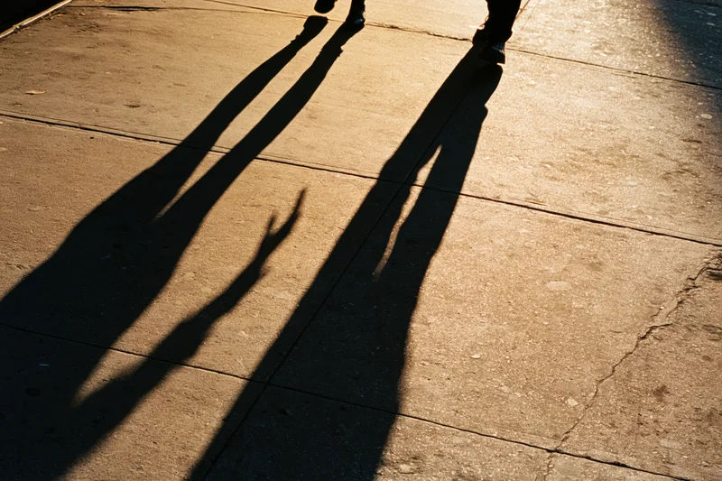 Long shadows of two people walking on a cracked concrete sidewalk in sunlight