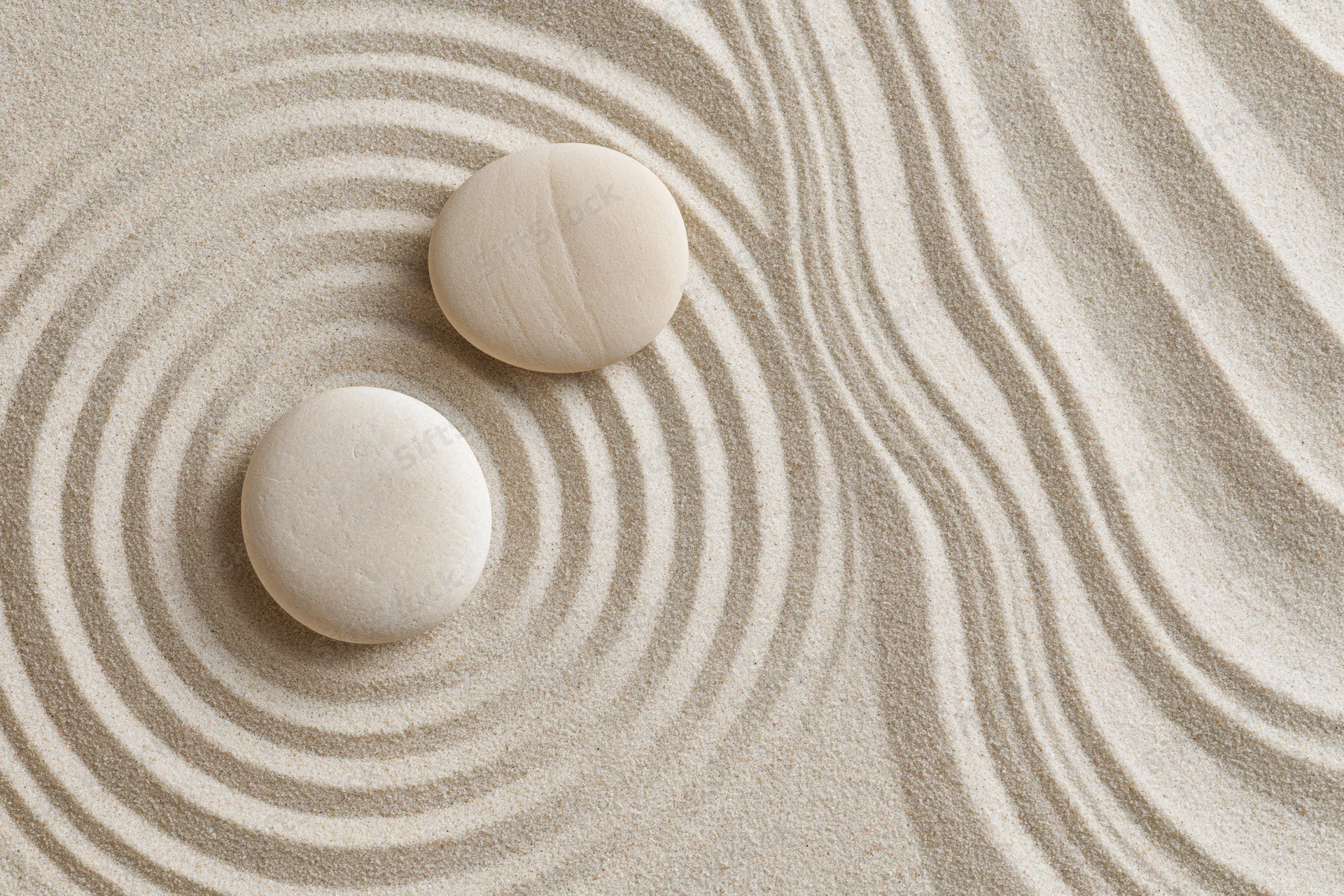 Two smooth white stones resting on raked sand in a zen garden