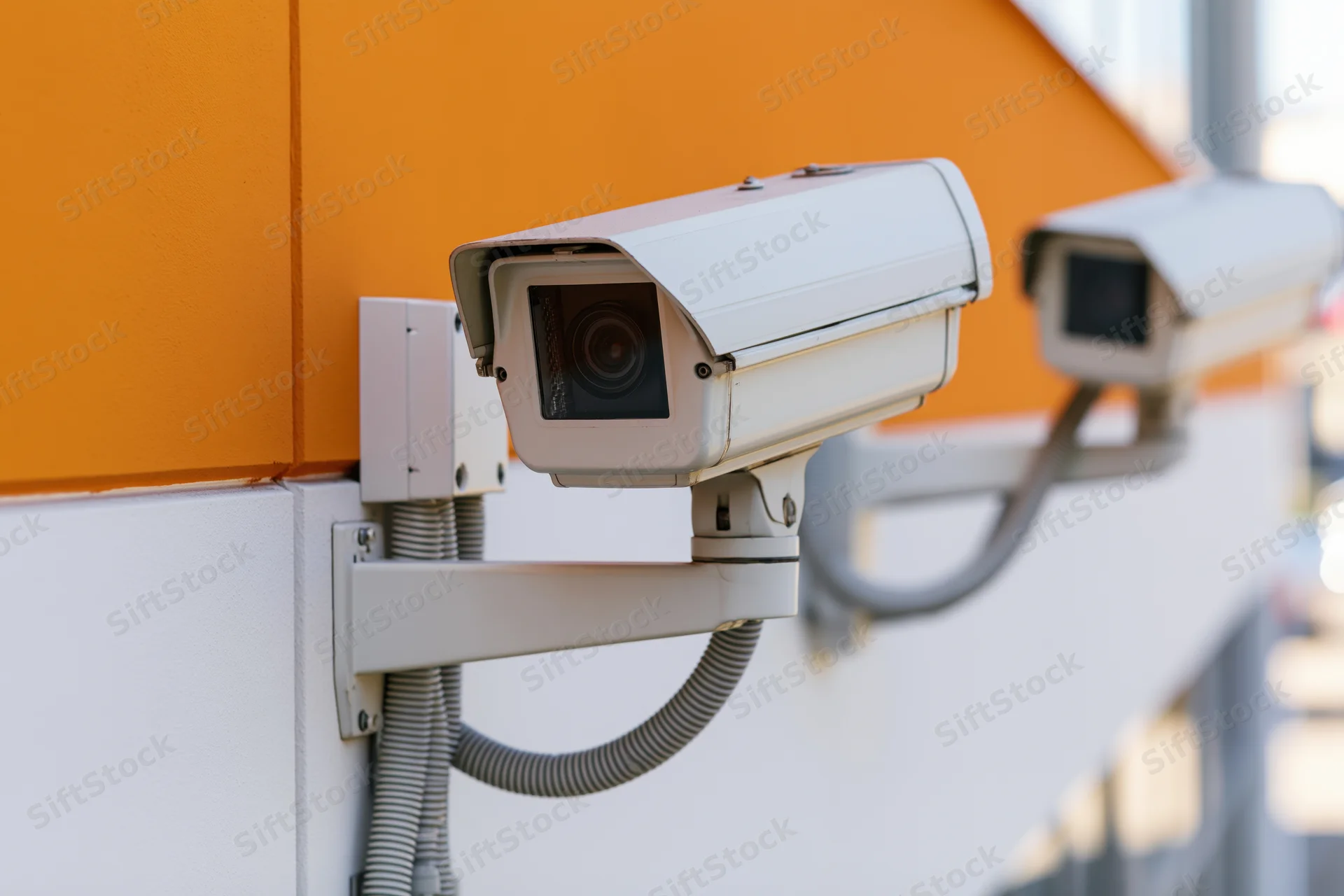 White cctv security cameras mounted on an orange and white wall outdoors