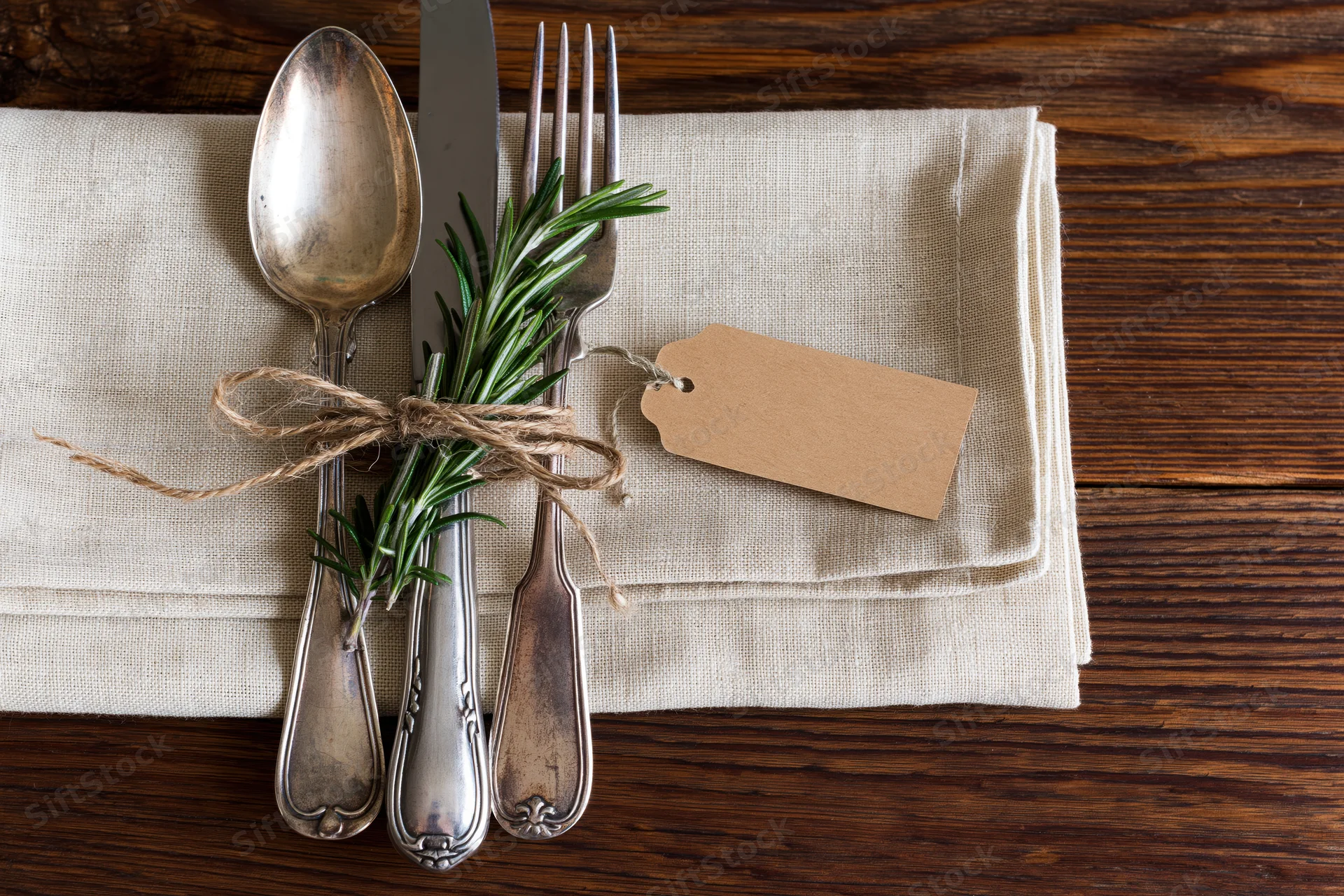 Vintage silver cutlery set tied with twine and rosemary on linen napkin on wooden table