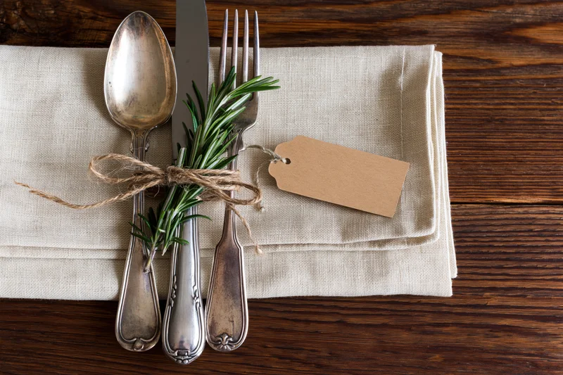 Vintage silver cutlery set tied with twine and rosemary on linen napkin on wooden table