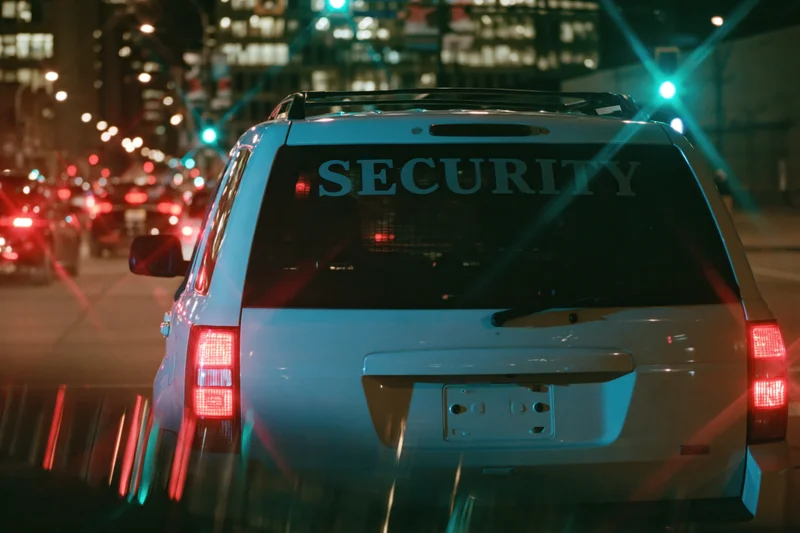 White suv with security lettering on rear windshield driving at night in city traffic