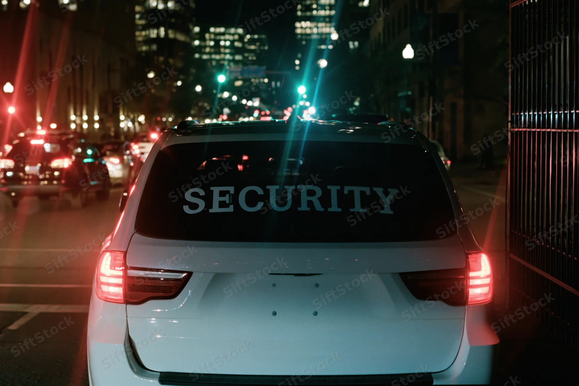 White suv with security lettering on rear windshield parked on city street at night