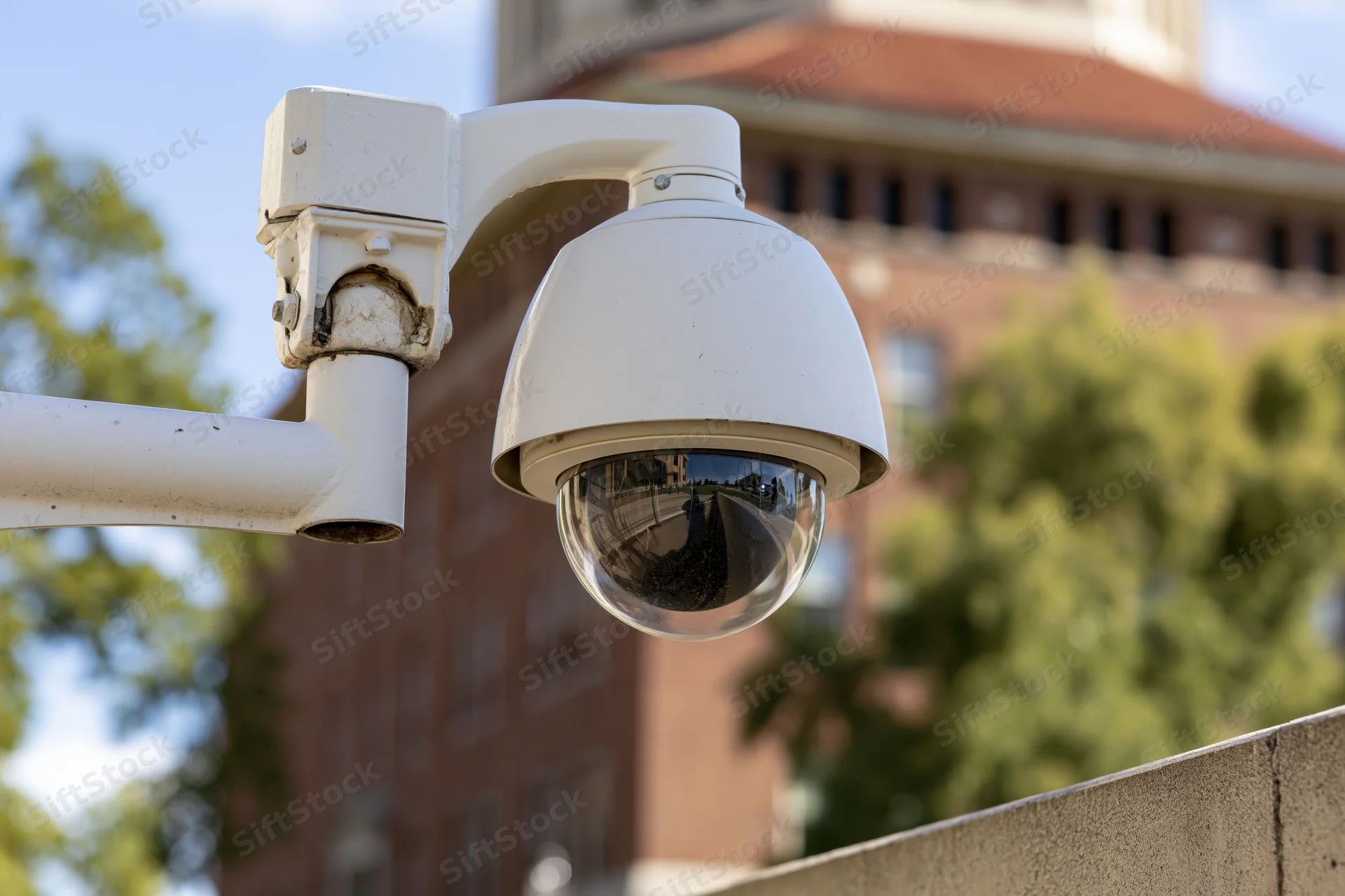White dome security camera mounted on metal arm outdoors near brick building