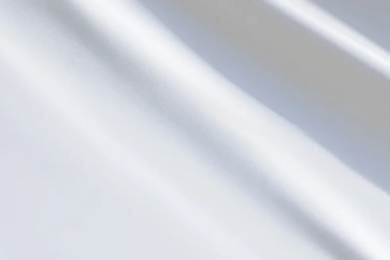 Soft white fabric with diagonal shadows and folds, creating a smooth textured surface