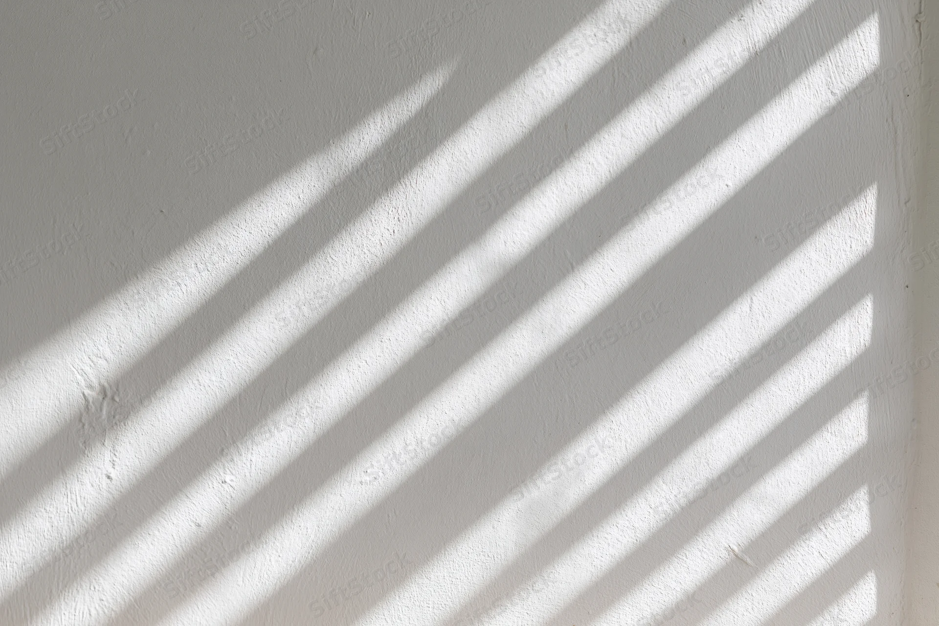Diagonal light streaks cast on a white plaster wall indoors